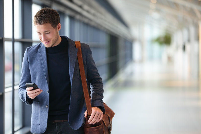 Man on smart phone - young business man in airport. Casual urban professional businessman using smar