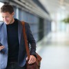 10 Apps For Frequent Travellers Man on smart phone - young business man in airport. Casual urban professional businessman using smar